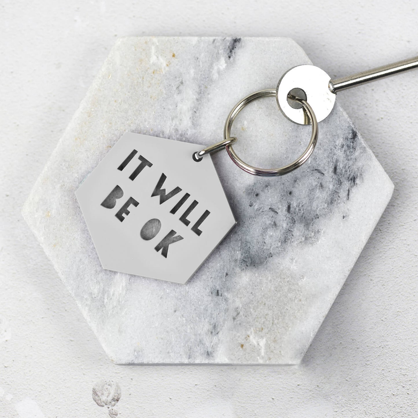 Grey Hexagonal keyring that says 'It will be ok' on a marble coaster