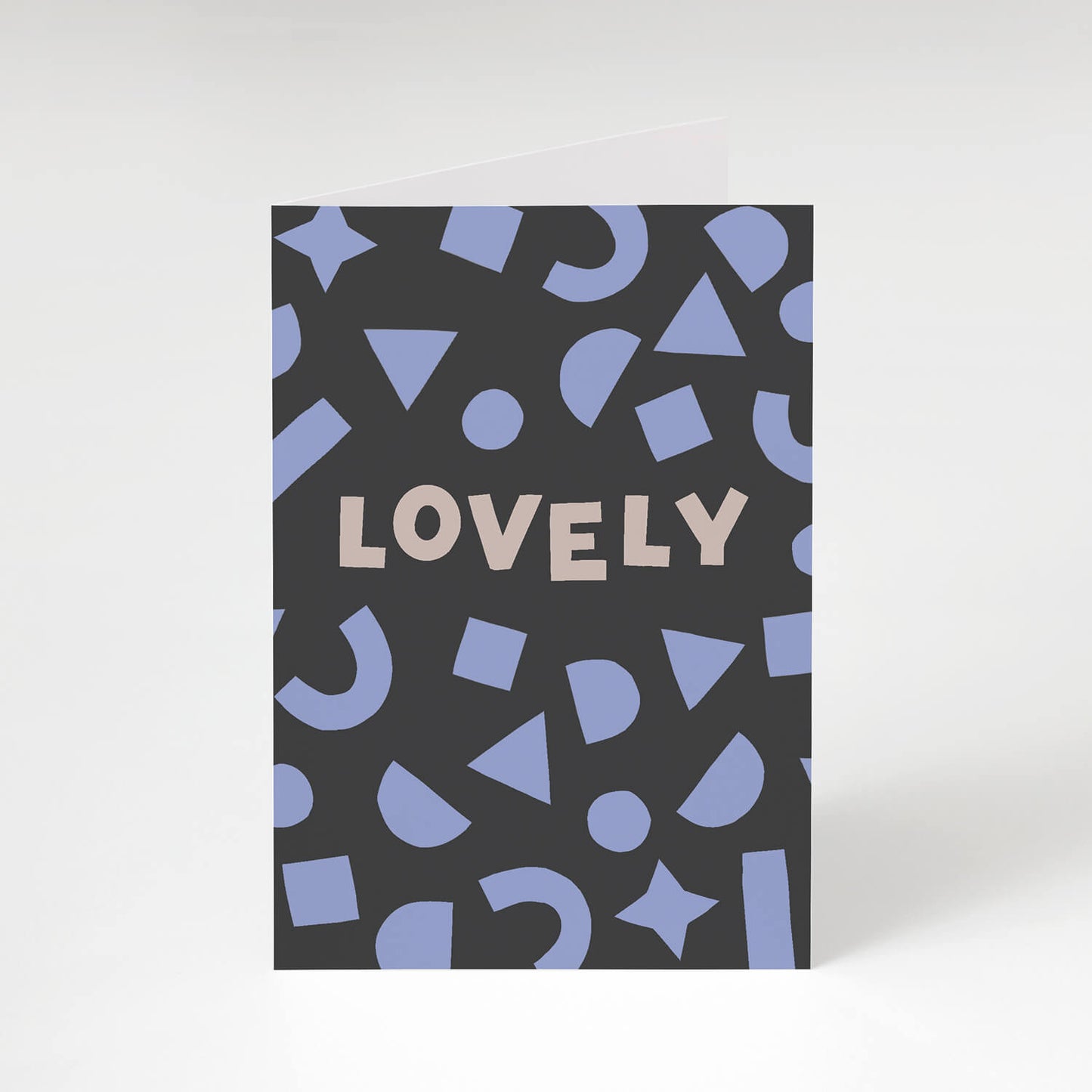 Playful celebrations greetings card featuring bold lilac shapes framing the hand lettered word 'Lovely' on a dark grey background