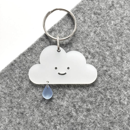 Keyring with a white cloud design and smiling face on a grey surface