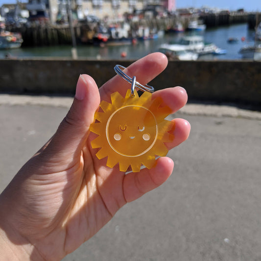 Hand holding a yellow sun-shaped keyring with a harbour in the background