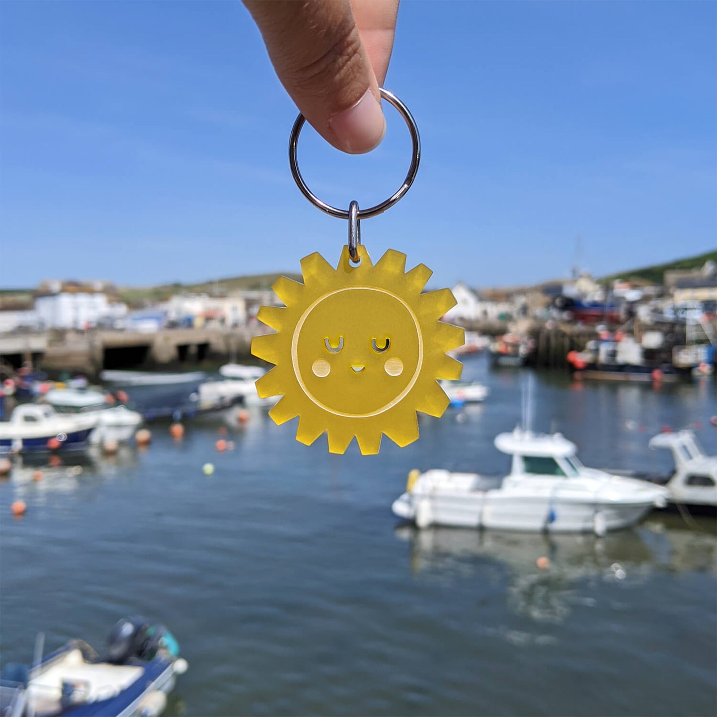 Yellow sun-shaped keyring held over a harbour with boats in the background.