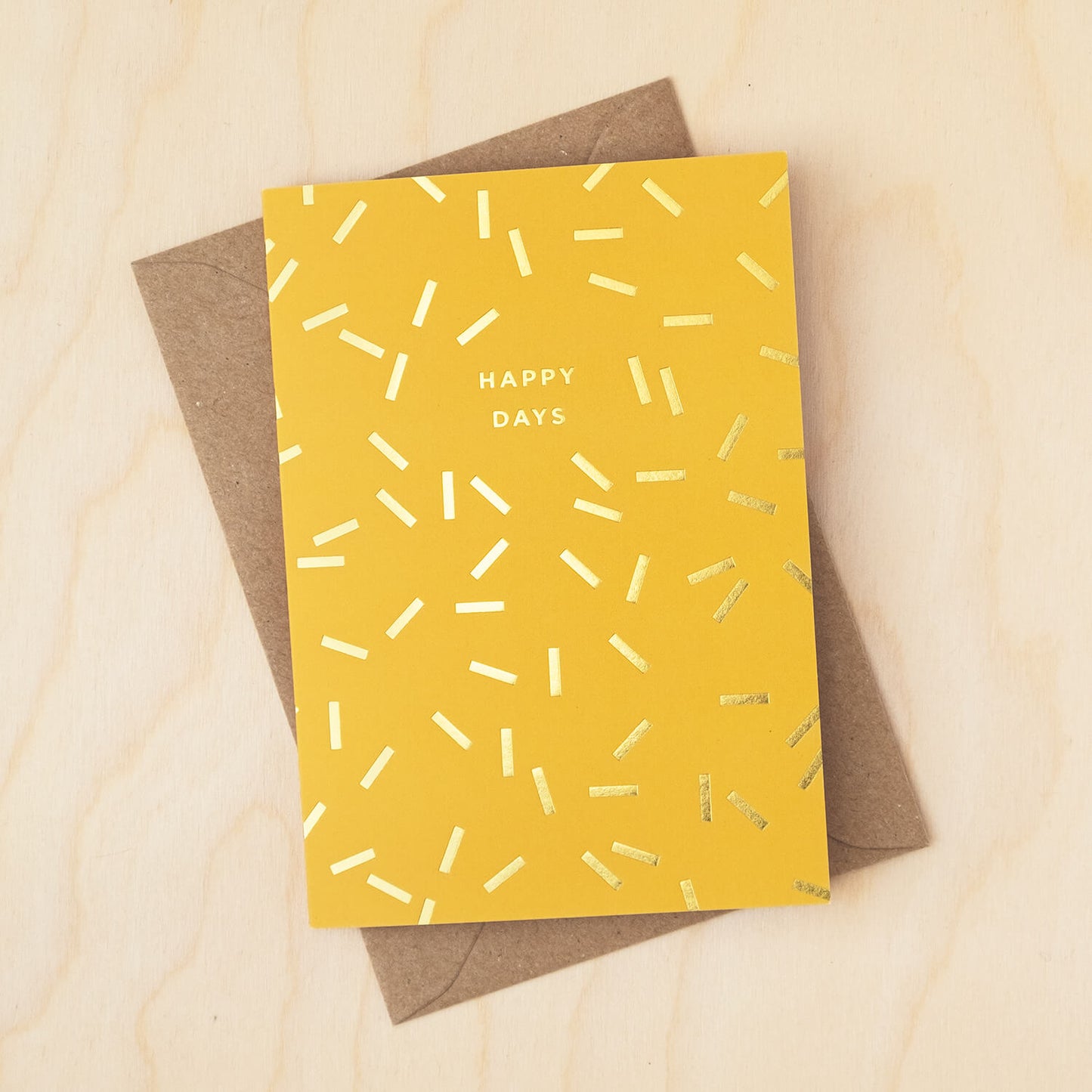 Yellow card covered in gold sprinkle shapes and a message that reads Happy Days