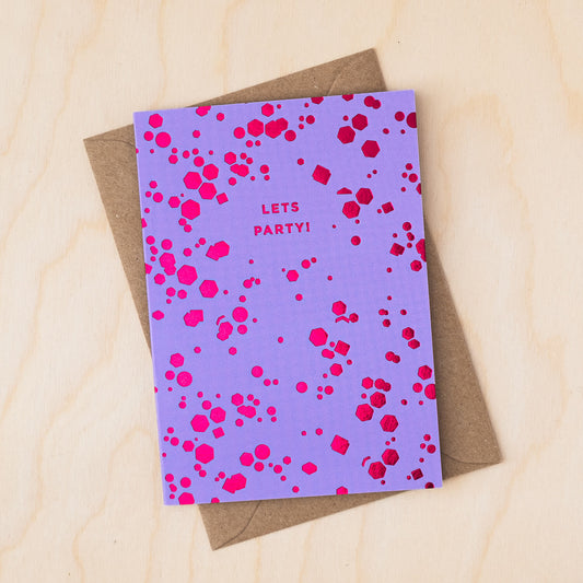 Purple card covered in pink foil confetti shapes and a message that reads Lets Party with a brown kraft envelope