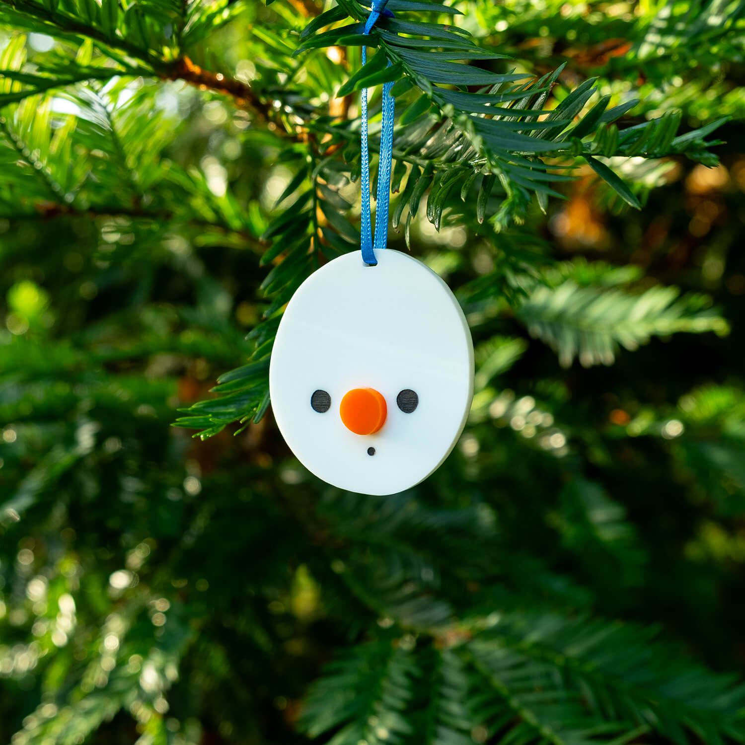 Cute snowman-shaped ornament hanging on a Christmas tree branch from a blue ribbon