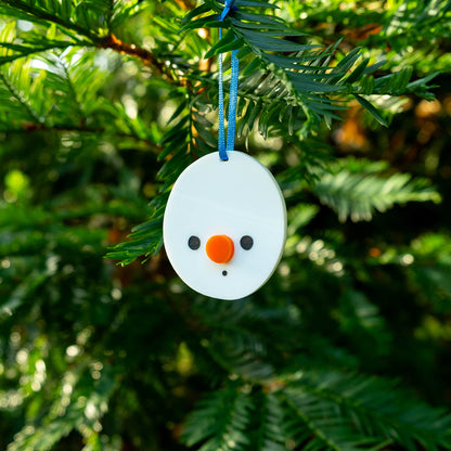 Cute snowman-shaped ornament hanging on a Christmas tree branch from a blue ribbon