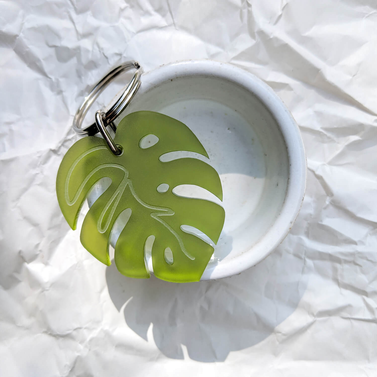 Green Monstera leaf-shaped keyring with engraved leaf details on a white dish with a white background