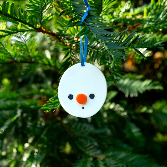 Round snowman Christmas decoration with a blue string and orange nose hanging on a tree
