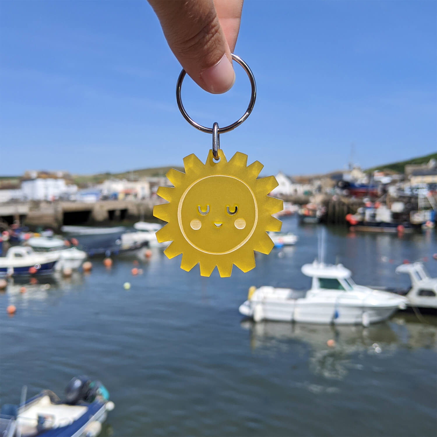 Yellow sun-shaped keyring held over a harbour with boats in the background.